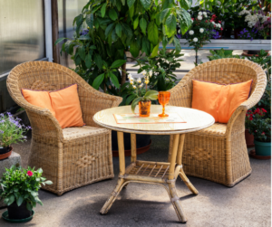 
Wicker patio set with two chairs and a table, featuring orange cushions and glasses, surrounded by potted plants.