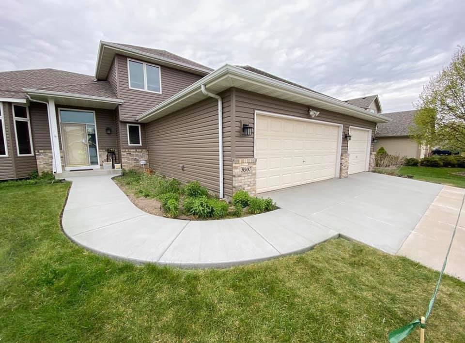 Newly installed concrete driveway and sidewalk in front of a modern two-story house with a two-car garage and landscaped yard in St. Michael, MN. 